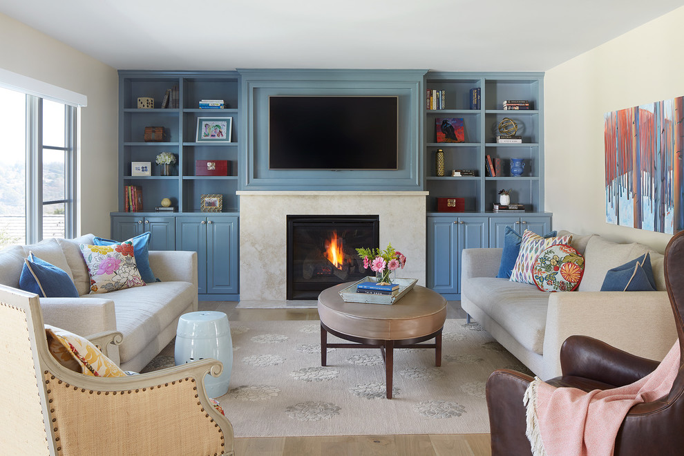 Example of a beach style light wood floor and beige floor living room library design in San Francisco with white walls, a standard fireplace and a media wall