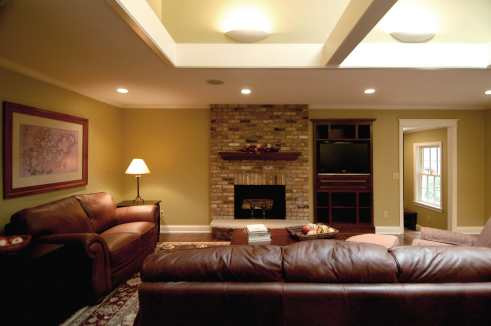 Klassisches Wohnzimmer mit grüner Wandfarbe, dunklem Holzboden, Kamin, Kaminumrandung aus Backstein und Multimediawand in Minneapolis