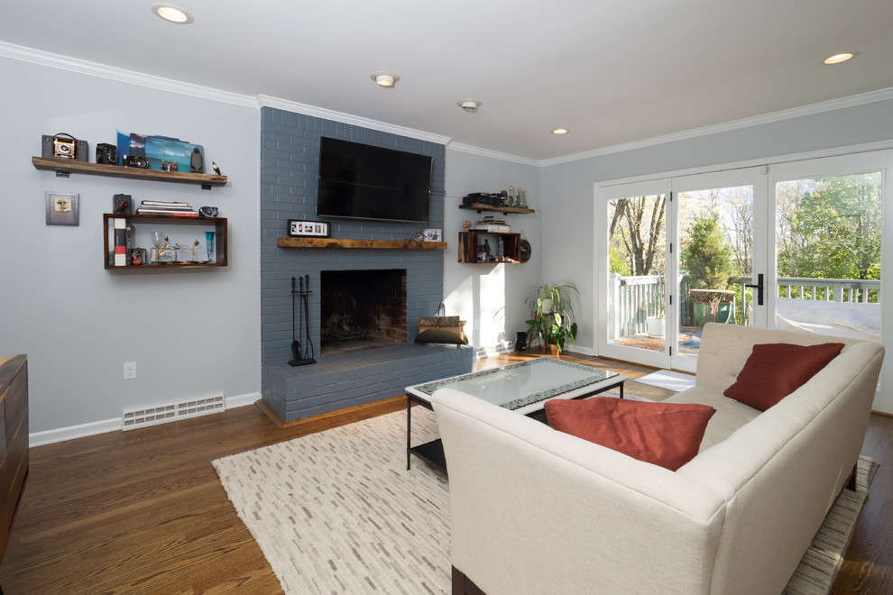 Modelo de sala de estar abierta clásica renovada de tamaño medio con paredes grises, suelo de madera en tonos medios, todas las chimeneas, marco de chimenea de ladrillo, televisor colgado en la pared y alfombra