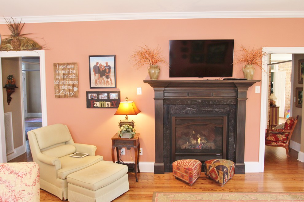 Mittelgroßes, Offenes Klassisches Wohnzimmer mit oranger Wandfarbe, braunem Holzboden, Tunnelkamin, Kaminumrandung aus Stein und TV-Wand in Sonstige