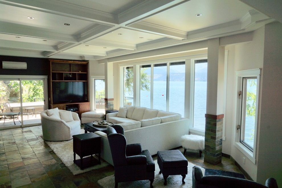 На фото: большая открытая гостиная комната в стиле неоклассика (современная классика) с белыми стенами, полом из сланца, двусторонним камином, фасадом камина из камня, мультимедийным центром и разноцветным полом