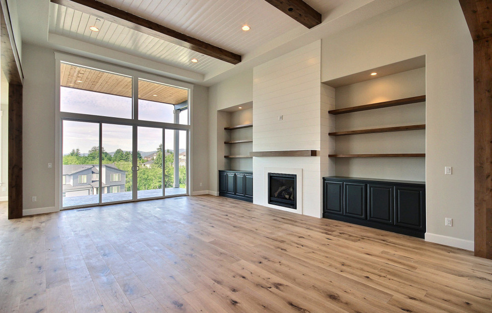 Expansive classic open plan games room in Portland with beige walls, light hardwood flooring, a standard fireplace, a timber clad chimney breast, a wall mounted tv, brown floors and exposed beams.