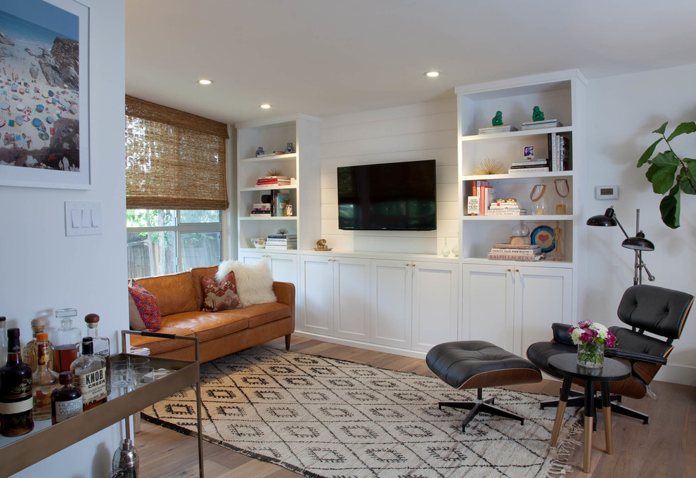 Пример оригинального дизайна: гостиная комната в стиле неоклассика (современная классика) с белыми стенами, телевизором на стене и коричневым диваном без камина