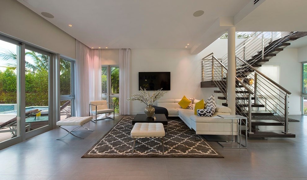 Modelo de sala de estar abierta moderna grande sin chimenea con paredes blancas, suelo de cemento, televisor colgado en la pared y suelo gris