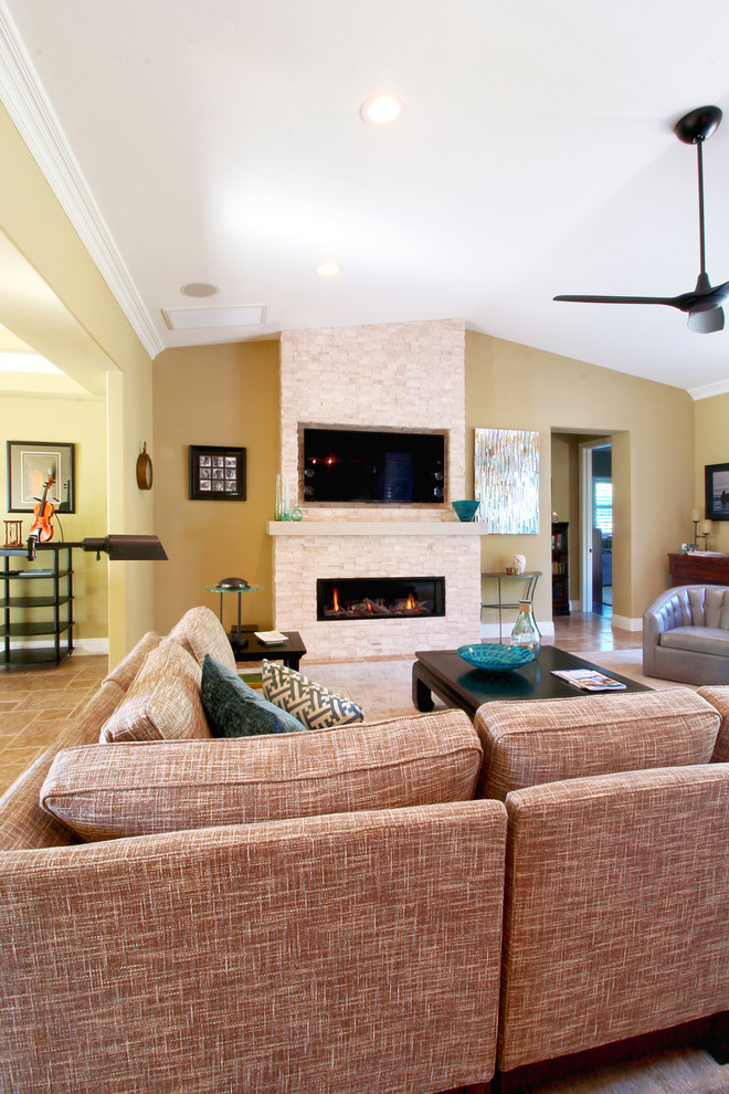 Modelo de sala de estar abierta costera grande con paredes amarillas, suelo de travertino, chimenea lineal, marco de chimenea de piedra y televisor colgado en la pared