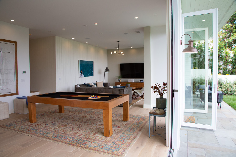 Photo of a large beach style open plan games room in Los Angeles with a game room, grey walls, light hardwood flooring, a standard fireplace, a stone fireplace surround, a built-in media unit and brown floors.