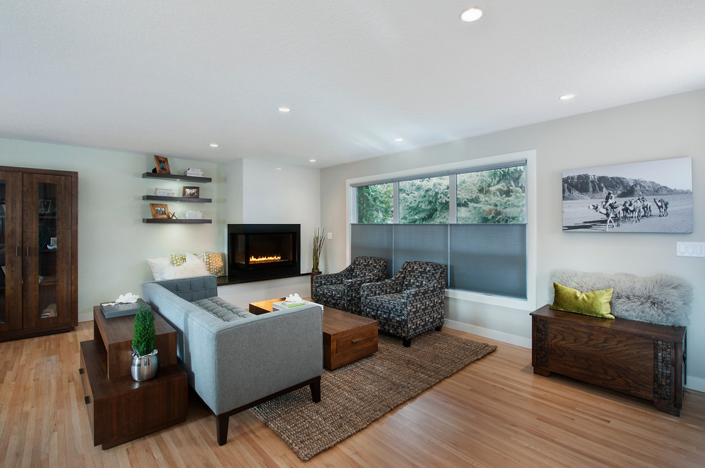 Diseño de sala de estar abierta contemporánea extra grande sin televisor con paredes grises, suelo de madera clara y chimenea de doble cara