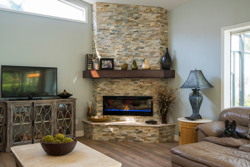 Aménagement d'une grande salle de séjour classique ouverte avec un mur gris, un sol en bois brun, une cheminée d'angle, un manteau de cheminée en pierre, un téléviseur indépendant et un sol marron.