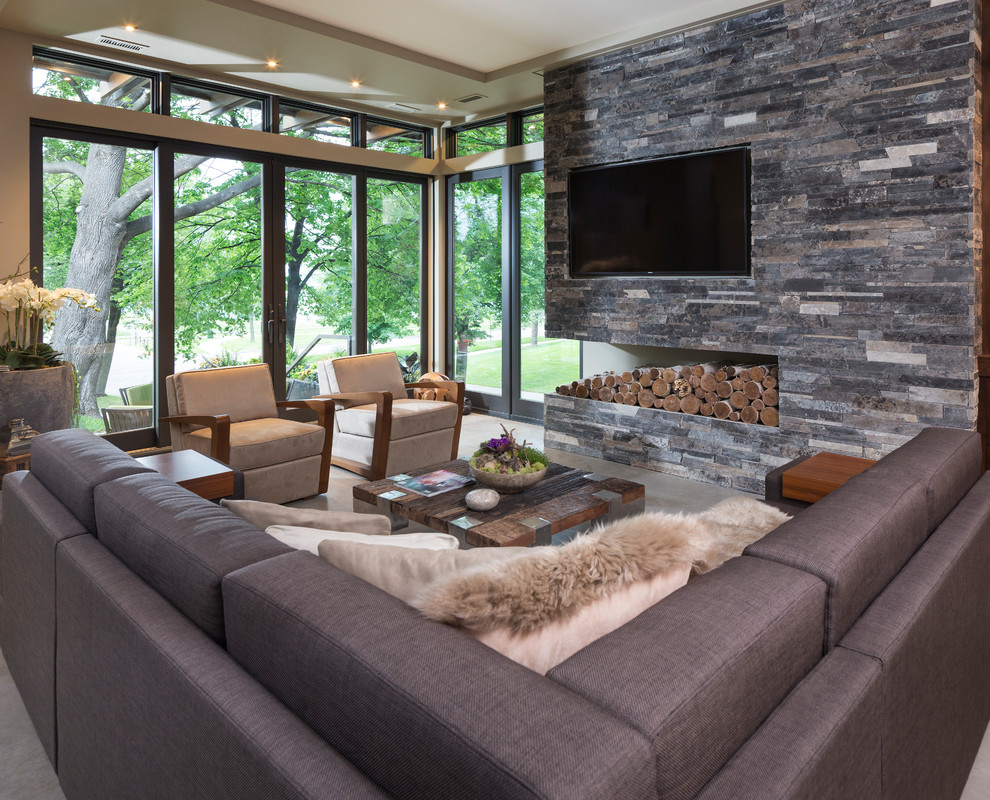 Modelo de sala de estar abierta moderna pequeña sin chimenea con paredes beige, suelo de cemento, marco de chimenea de piedra y televisor colgado en la pared