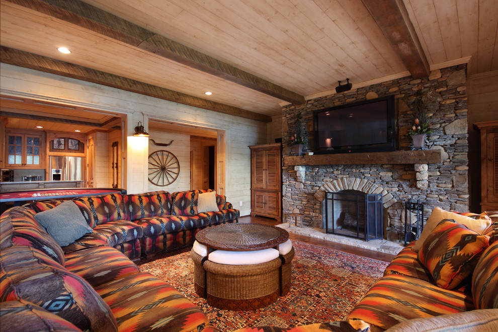 На фото: большая открытая гостиная комната в стиле рустика с стандартным камином, фасадом камина из камня, телевизором на стене, бежевыми стенами, паркетным полом среднего тона, коричневым полом и ковром на полу
