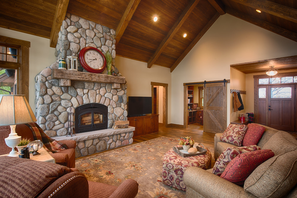 Design ideas for a large rustic enclosed games room in Minneapolis with a standard fireplace, a stone fireplace surround, beige walls, medium hardwood flooring and a freestanding tv.