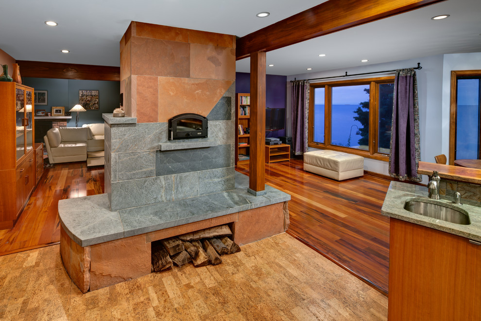 Modelo de sala de estar abierta contemporánea extra grande con suelo de corcho, chimenea de doble cara, marco de chimenea de piedra y televisor colgado en la pared