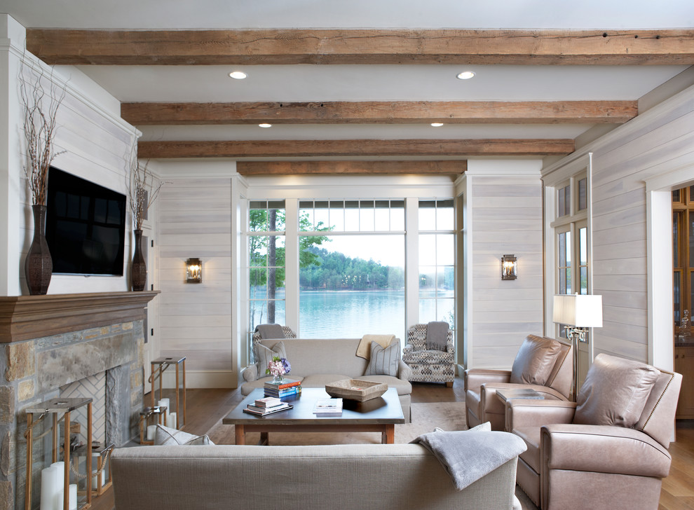 Diseño de sala de estar marinera con paredes beige, suelo de madera en tonos medios, todas las chimeneas, marco de chimenea de piedra y televisor colgado en la pared