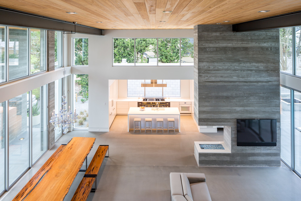 Diseño de sala de estar abierta minimalista extra grande con paredes blancas, suelo de cemento, chimenea de doble cara, marco de chimenea de hormigón y televisor colgado en la pared