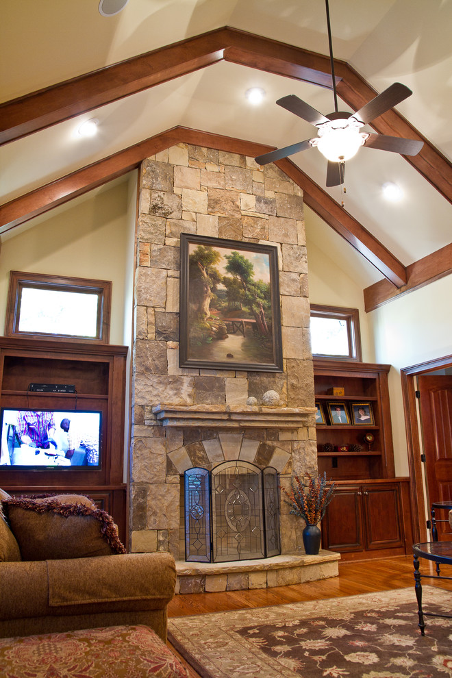 Foto de sala de estar abierta tradicional de tamaño medio con paredes beige, suelo de madera oscura, todas las chimeneas, marco de chimenea de piedra y televisor retractable