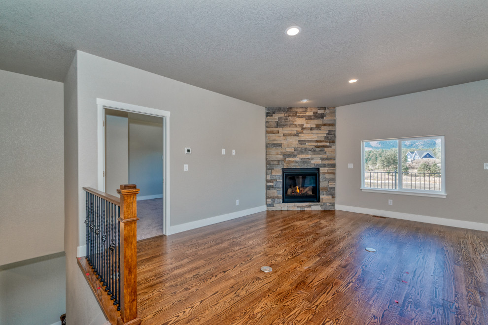 Ejemplo de sala de estar de estilo americano de tamaño medio con paredes grises, suelo de madera en tonos medios, chimenea de esquina, piedra de revestimiento y suelo marrón