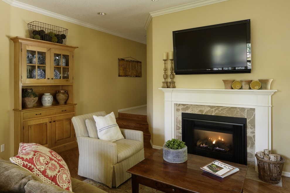 Modelo de sala de estar tipo loft clásica de tamaño medio con paredes amarillas, suelo de madera en tonos medios, todas las chimeneas, marco de chimenea de hormigón y televisor colgado en la pared