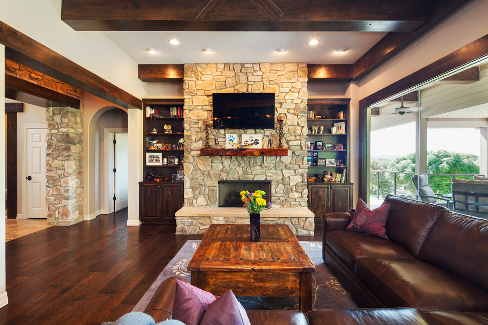 Großes, Offenes Klassisches Wohnzimmer mit beiger Wandfarbe, dunklem Holzboden, Kamin, Kaminumrandung aus Stein, TV-Wand und braunem Boden in Austin