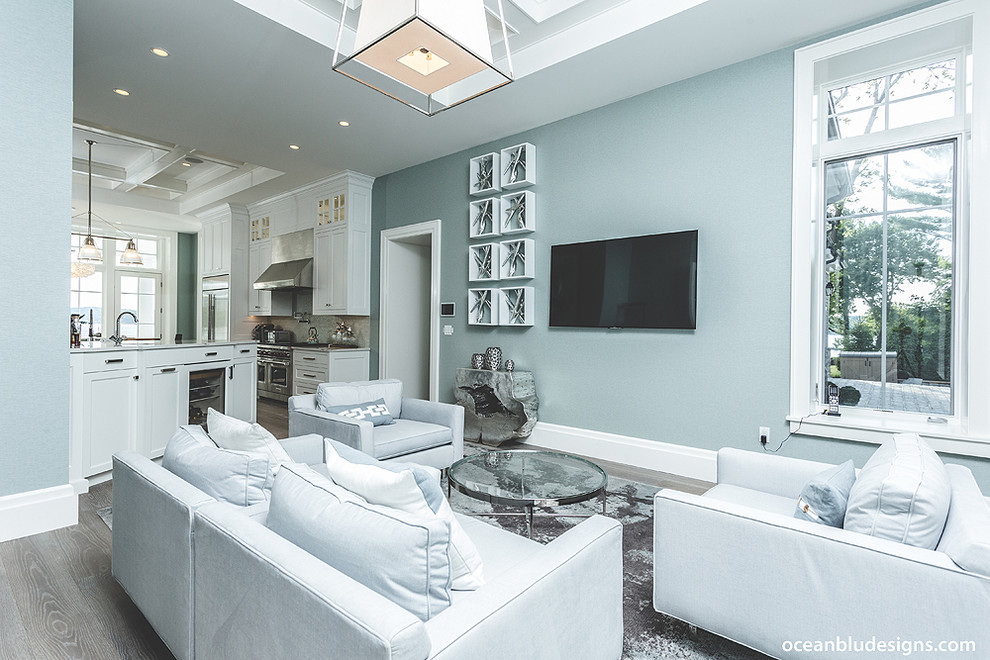 Diseño de sala de estar abierta actual de tamaño medio con paredes azules, suelo de madera clara y televisor colgado en la pared