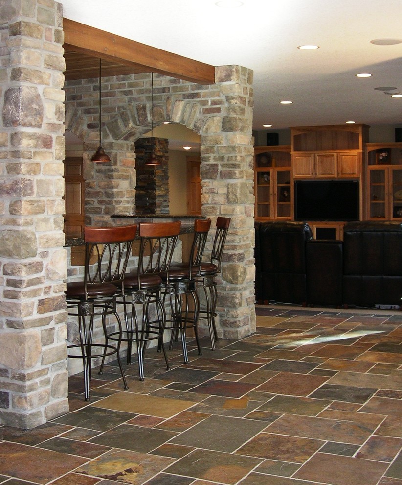 Cette image montre une grande salle de séjour traditionnelle ouverte avec un bar de salon, un mur beige, un sol en ardoise, une cheminée standard, un manteau de cheminée en pierre et un téléviseur encastré.