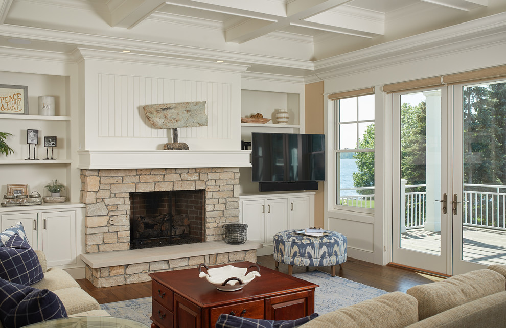 Пример оригинального дизайна: гостиная комната в классическом стиле с бежевыми стенами, паркетным полом среднего тона, стандартным камином, фасадом камина из камня, телевизором в углу, коричневым полом и кессонным потолком
