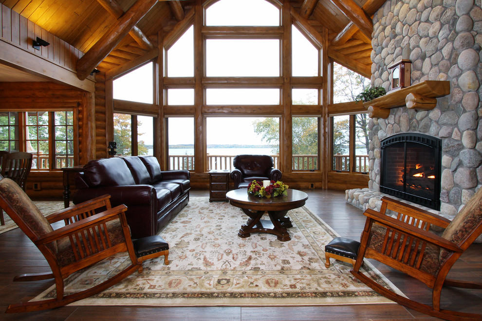 This is an example of a medium sized rustic open plan games room in Other with white walls, dark hardwood flooring, a standard fireplace, a stone fireplace surround, a wall mounted tv and brown floors.