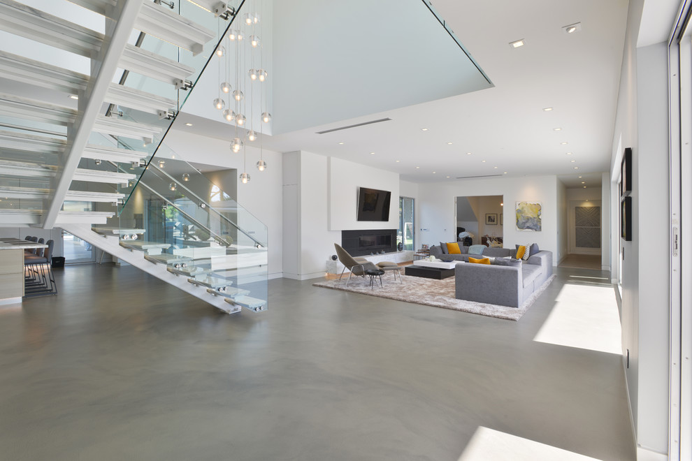 Imagen de sala de estar abierta moderna grande con paredes blancas, suelo de cemento, chimenea lineal, marco de chimenea de metal y televisor colgado en la pared