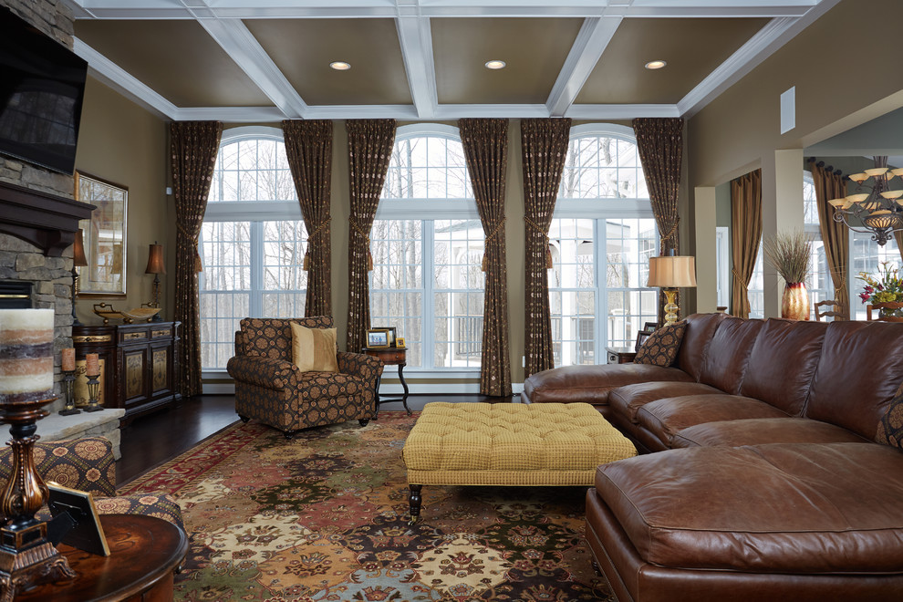 Стильный дизайн: большая гостиная комната в классическом стиле с коричневыми стенами, темным паркетным полом, двусторонним камином, фасадом камина из камня и телевизором на стене - последний тренд