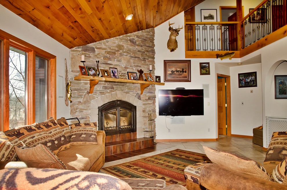 Foto de sala de estar abierta rústica grande con paredes blancas, suelo de baldosas de cerámica, estufa de leña, marco de chimenea de piedra, televisor colgado en la pared y suelo beige