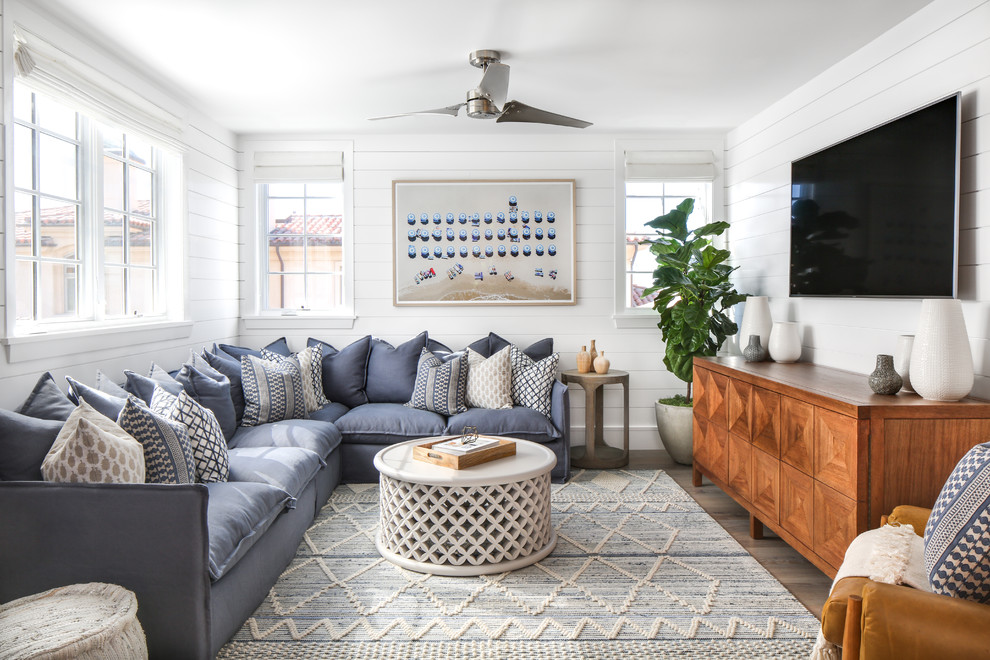 Diseño de sala de estar costera con paredes blancas, suelo de madera en tonos medios, televisor colgado en la pared, suelo marrón y alfombra