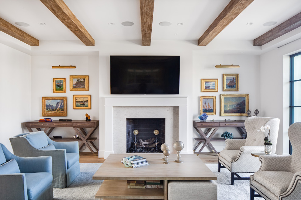 Imagen de sala de estar costera con paredes blancas, suelo de madera clara, todas las chimeneas, marco de chimenea de piedra y televisor colgado en la pared
