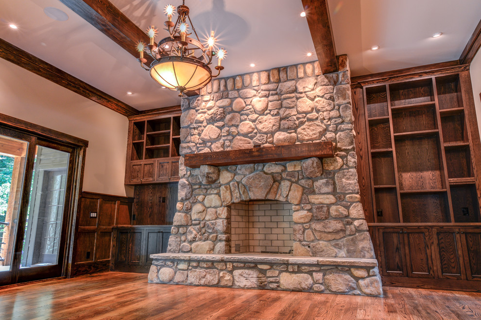 Inspiration for a large rustic enclosed games room in Other with beige walls, dark hardwood flooring, a standard fireplace, a stone fireplace surround, no tv and brown floors.