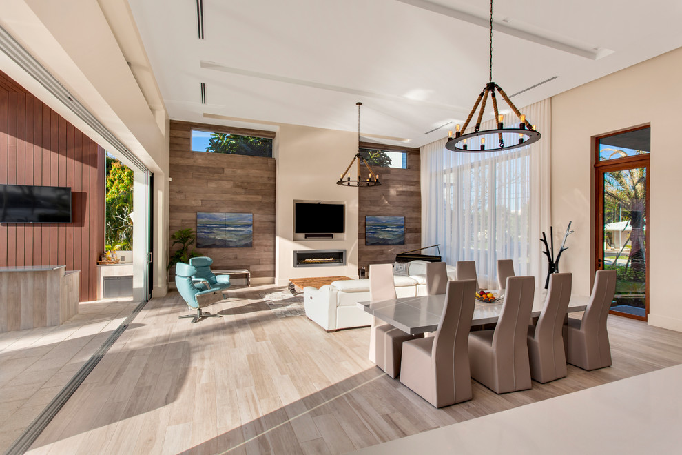 Contemporary open plan games room in Miami with beige walls, a ribbon fireplace, a metal fireplace surround, a wall mounted tv and beige floors.