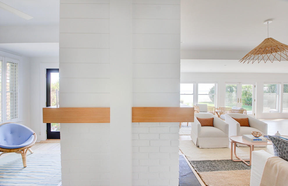 Modelo de sala de estar machihembrado y abierta marinera grande con paredes blancas, suelo de madera clara, chimenea de doble cara y televisor colgado en la pared