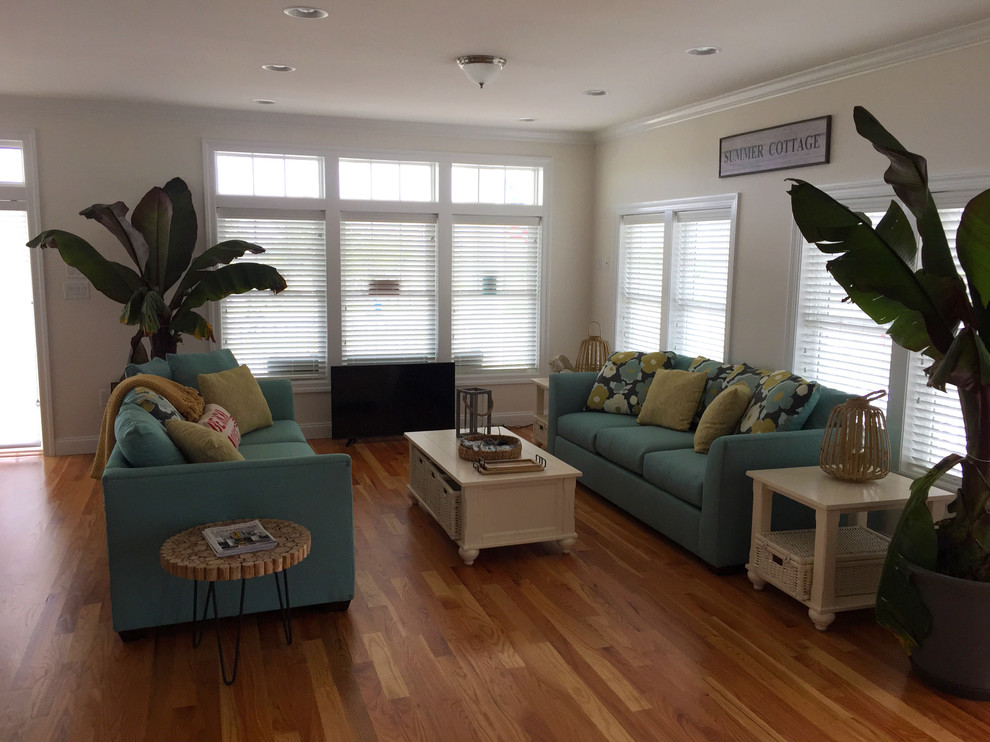 Immagine di un ampio soggiorno stile marino aperto con pareti beige, pavimento in legno massello medio, nessun camino e TV autoportante