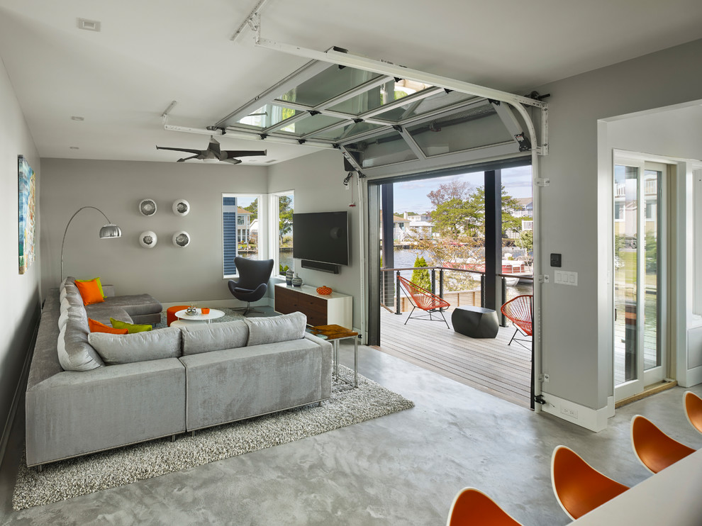 Foto de sala de estar abierta contemporánea pequeña sin chimenea con paredes grises, suelo de cemento, televisor colgado en la pared y suelo gris