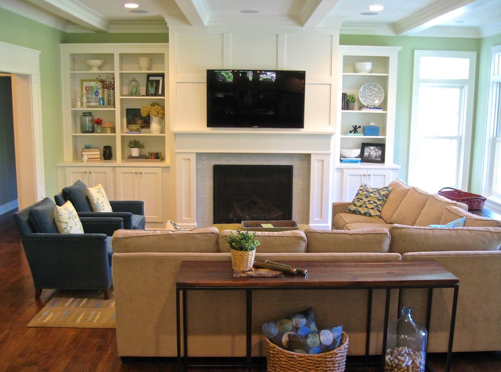Modelo de sala de estar abierta tradicional renovada con paredes verdes, suelo de madera en tonos medios, todas las chimeneas, marco de chimenea de baldosas y/o azulejos y televisor colgado en la pared