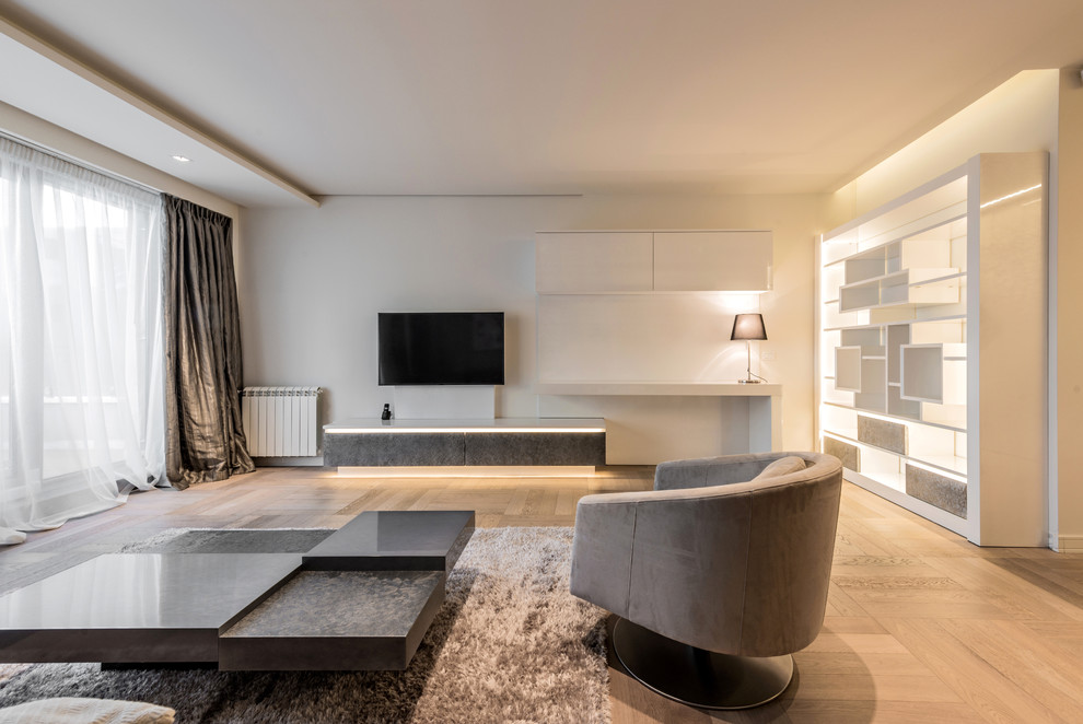Diseño de sala de estar abierta moderna extra grande sin chimenea con paredes blancas, suelo de madera clara, televisor colgado en la pared y suelo marrón