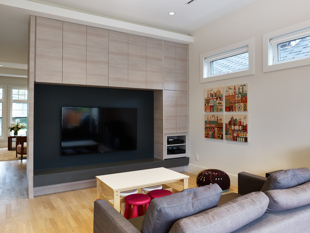 Foto de sala de estar abierta actual sin chimenea con paredes beige, suelo de madera clara y pared multimedia