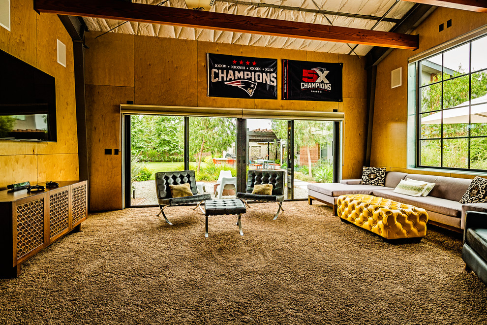 Пример оригинального дизайна: большая открытая комната для игр в стиле ретро с желтыми стенами, ковровым покрытием, телевизором на стене и коричневым полом без камина