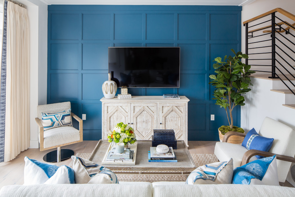 Пример оригинального дизайна: открытая гостиная комната в морском стиле с синими стенами, светлым паркетным полом и телевизором на стене