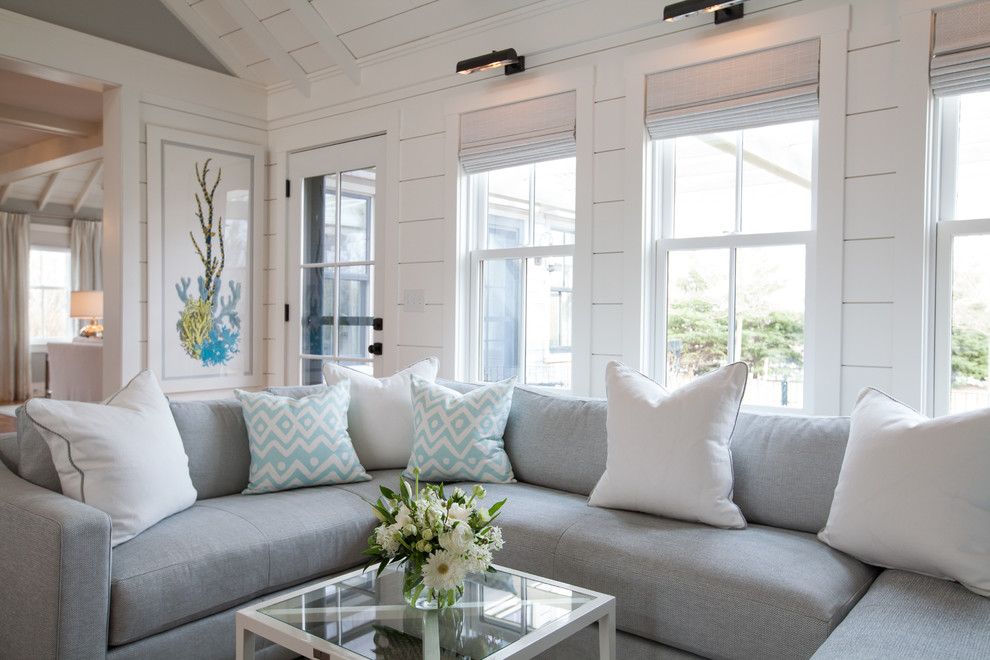 Imagen de sala de estar abierta costera grande con paredes grises, suelo de madera clara, todas las chimeneas y televisor colgado en la pared