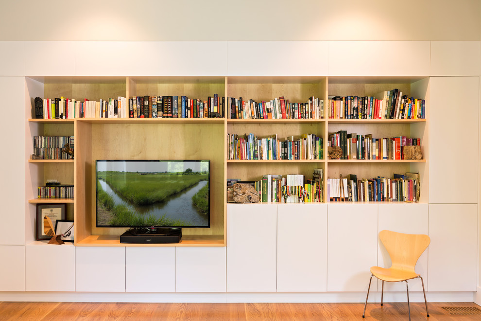 Foto de sala de estar con biblioteca cerrada moderna de tamaño medio con paredes beige, suelo de madera en tonos medios, pared multimedia y suelo beige