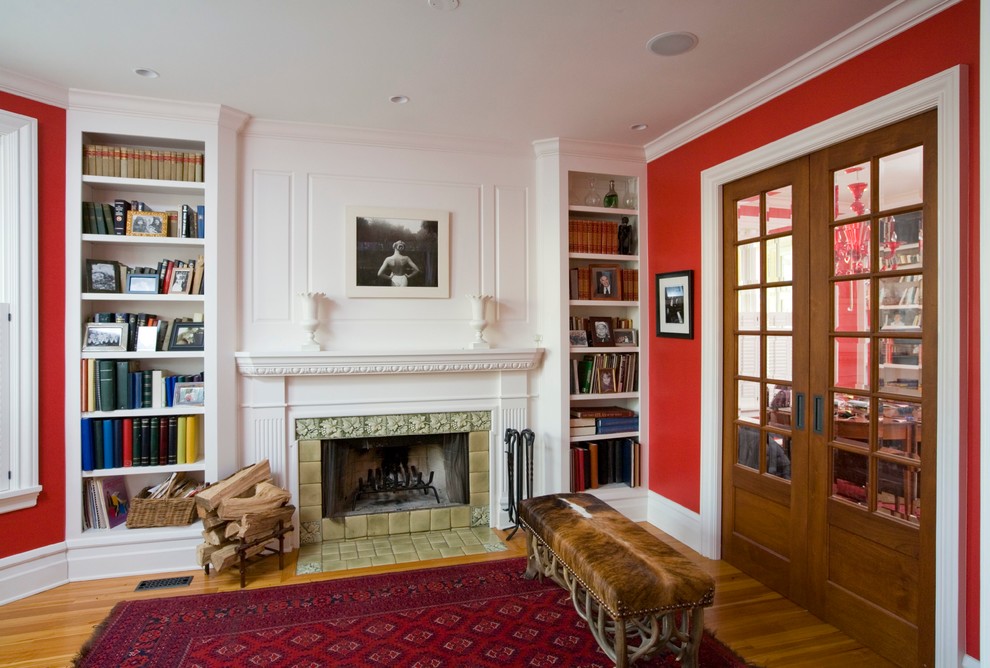 Imagen de sala de estar con biblioteca cerrada de estilo americano de tamaño medio sin televisor con paredes rojas, suelo de madera clara, todas las chimeneas y marco de chimenea de baldosas y/o azulejos