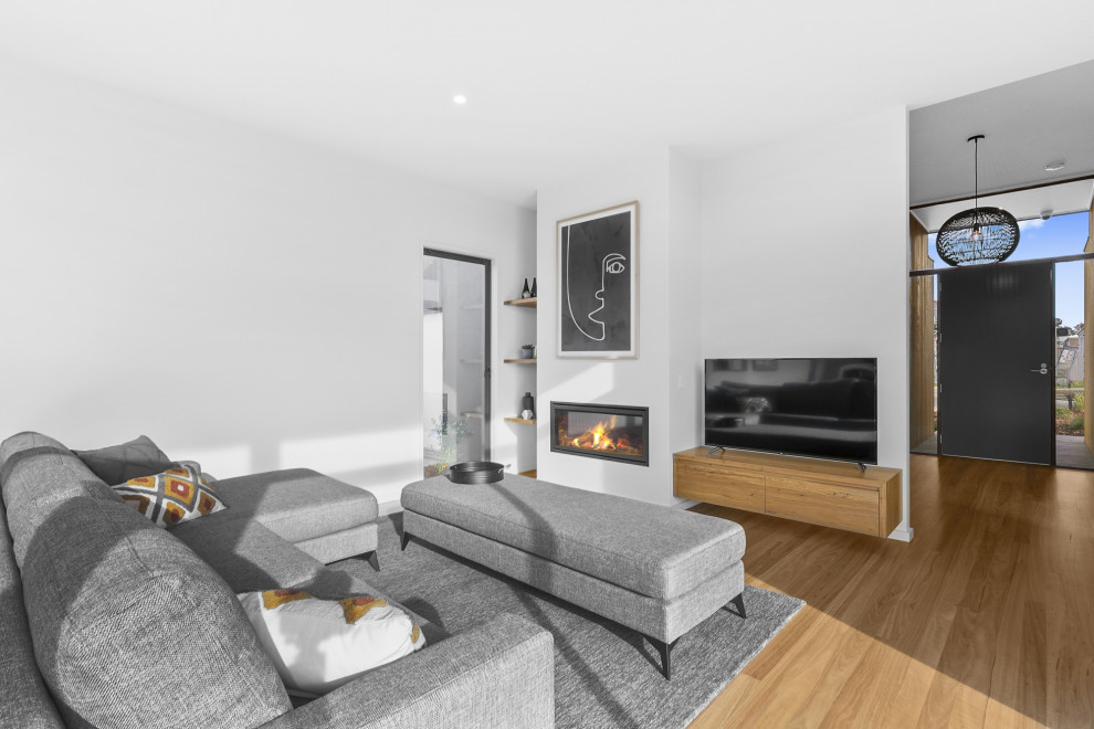 Imagen de sala de estar abierta contemporánea de tamaño medio con paredes blancas, suelo de madera clara, todas las chimeneas, marco de chimenea de yeso y televisor independiente
