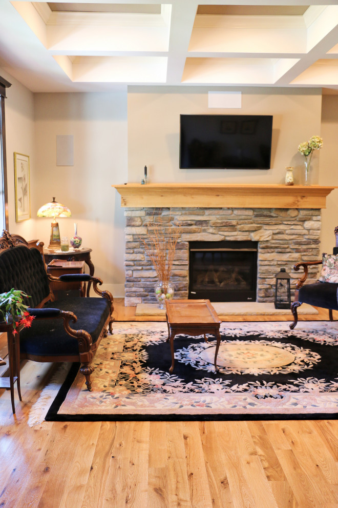 Cette image montre une grande salle de séjour traditionnelle ouverte avec un mur blanc, un sol en bois brun, une cheminée standard, un manteau de cheminée en pierre, un téléviseur fixé au mur et un sol marron.
