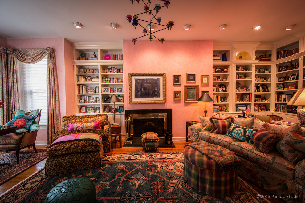 Immagine di un grande soggiorno eclettico chiuso con pareti rosa, camino classico, cornice del camino in pietra, pavimento in legno massello medio e libreria