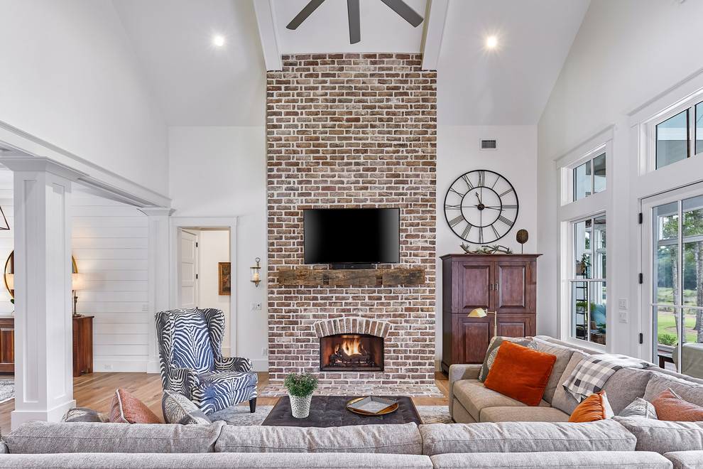 Offenes, Großes Maritimes Wohnzimmer mit weißer Wandfarbe, hellem Holzboden, Kaminumrandung aus Backstein, TV-Wand und Kamin in Charleston