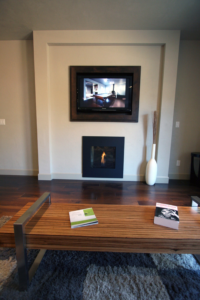 Imagen de sala de estar abierta minimalista de tamaño medio con paredes grises, suelo de madera en tonos medios, todas las chimeneas y pared multimedia