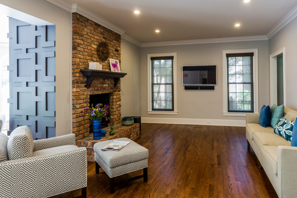 Cette image montre une salle de séjour traditionnelle de taille moyenne et ouverte avec un mur gris, un sol en bois brun, une cheminée standard, un manteau de cheminée en brique et un téléviseur fixé au mur.